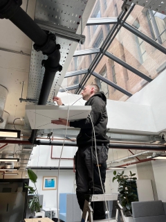 Technician installing Sennheiser ceiling microphone in BCS London atrium.